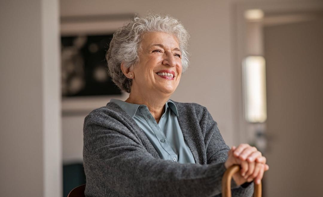 elderly woman with a cane, sits in a room and smiles